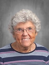 Portrait of a smiling elderly woman with short gray hair and glasses, wearing a striped shirt.