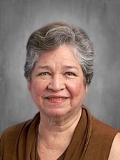 Portrait of a smiling older woman with short gray hair, wearing a brown sleeveless top.