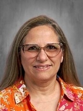 Portrait of a smiling woman with shoulder-length hair, wearing an orange floral shirt and glasses.