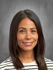 Portrait of a smiling woman with shoulder-length dark hair wearing a white and black striped shirt against a neutral gray background.