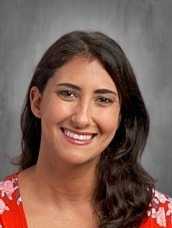 Smiling woman with dark hair wearing a red floral blouse against a gray studio backdrop.