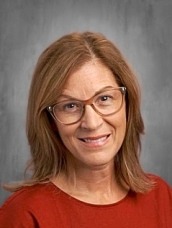 Portrait of a smiling woman with shoulder-length light brown hair, glasses, and a red top against a gray studio backdrop.