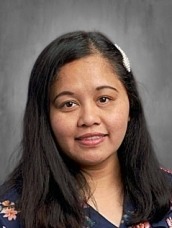 Portrait of a woman with long dark hair wearing a navy floral blouse against a gray studio backdrop.