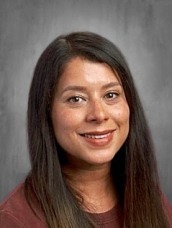 Head-and-shoulders portrait of a smiling woman with long dark hair wearing a maroon top against a gray background.