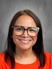 Head-and-shoulders portrait of a smiling woman with dark hair, glasses, and an orange top facing the camera.