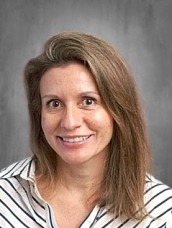 Head-and-shoulders portrait of a smiling woman with light brown hair in a striped shirt against a gray backdrop.