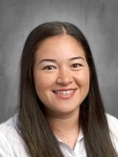 Portrait of a smiling woman with long dark hair wearing a white blouse.