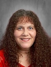 Portrait of a smiling woman with long curly brown hair wearing a red blouse.
