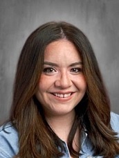 Professional headshot of a smiling woman in a navy blazer against a gray background, suitable for LinkedIn or corporate profiles.