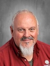 Portrait of a smiling older man with gray hair and a white goatee, wearing a red shirt.