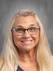 Smiling woman with long blonde hair and glasses, posed against a gray backdrop.